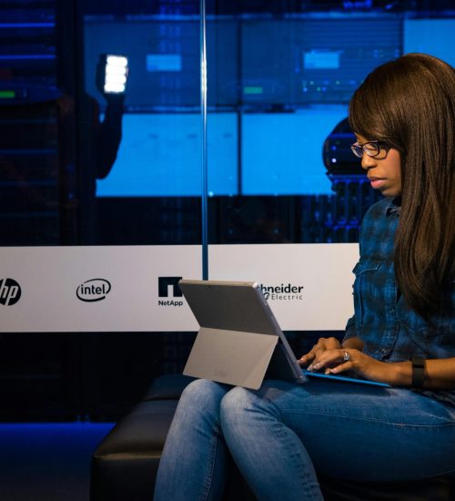 Professional woman working on laptop in a server room, showcasing technology and remote work.