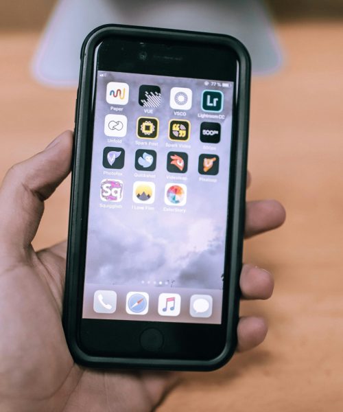 A close-up image of a hand holding a smartphone with various app icons visible on the screen.