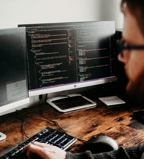 Focused software developer at desk coding with multiple monitors in a modern workspace.